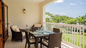 A balcony with wicker furniture, a table set for dining, and a view of a lush landscape.