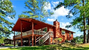 A two-story wooden house with a balcony and a staircase leading to the upper floor. - Lake Front Cabin! 
Pool, Basketball, Boat parking & Firepit. Lots of parking. (Brookeland)