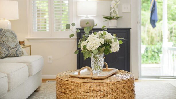 A living room with a white sofa, a wicker side table with a vase of flowers, and a fireplace in the background. - Historic Annapolis Home! (Annapolis)