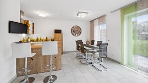 A modern kitchen with a dining area, featuring a bar stool, a dining table with chairs, a television mounted above the counter, and a clock on the wall. - 2 bedroom nice home in Rotthalmünster (Rotthalmünster)