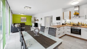 A modern kitchen with white cabinets, a built-in oven, and a dining area with a glass table and wicker chairs. - 2 bedroom nice home in Rotthalmünster (Rotthalmünster)