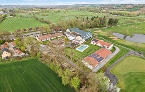 Vista aérea de un campo de golf con un club de campo, una piscina y campos verdes circundantes.