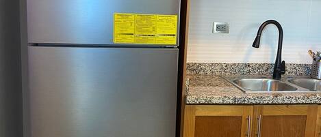 Ein Edelstahl-Kühlschrank mit einem gelben Aufkleber, Holzschränke und eine Arbeitsplatte aus Granit mit einem schwarzen Wasserhahn.