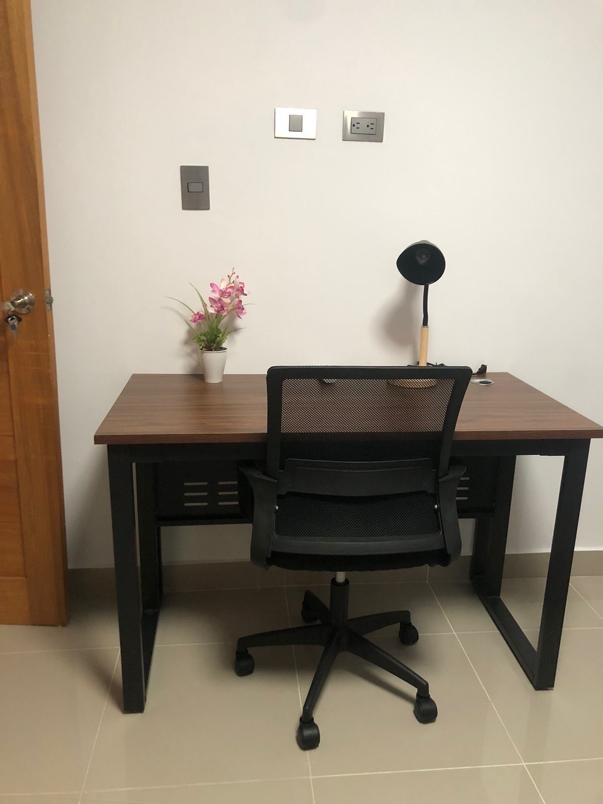 Een bureau met een stoel, een potplant, een lamp en stopcontacten aan de muur.