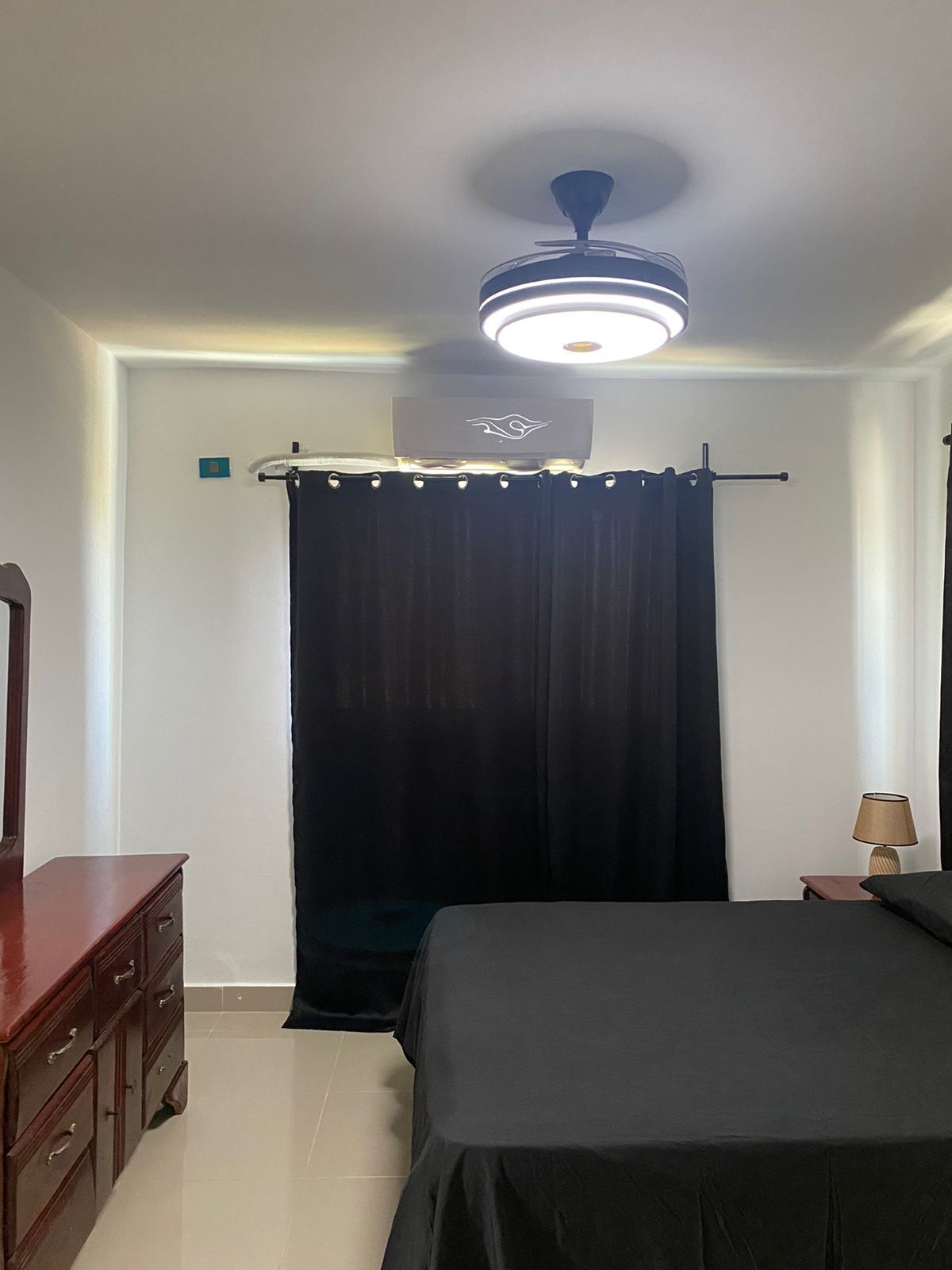 Une chambre à coucher avec un lit, une commode, un ventilateur de plafond et une lampe.