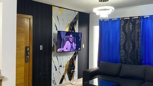 Un salon moderne avec un téléviseur à écran plat fixé au mur, un mur au motif de marbre, un canapé de couleur foncée et un rideau bleu.