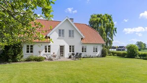 A white house with a red-tiled roof, a front lawn, and a garden area with outdoor furniture. - Nice home in Sønderborg with kitchen (Sønderborg)