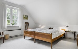 A bedroom with a wooden bed, a bedside table with a lamp, a chair, and a window with curtains. - Nice home in Sønderborg with kitchen (Sønderborg)