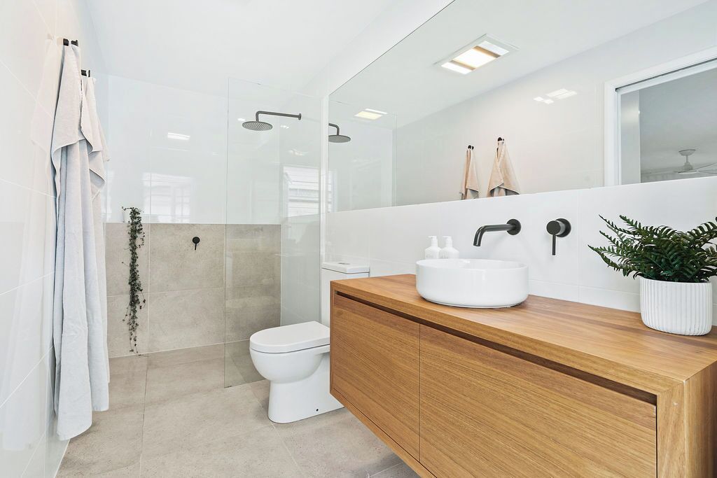 Ein modernes Badezimmer mit einer Duschkabine aus Glas, einer weißen Toilette und einem hölzernen Waschtisch mit weißem Becken.