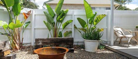 A backyard with a white fence, a wooden bench, a metal planter, and a wicker chair.