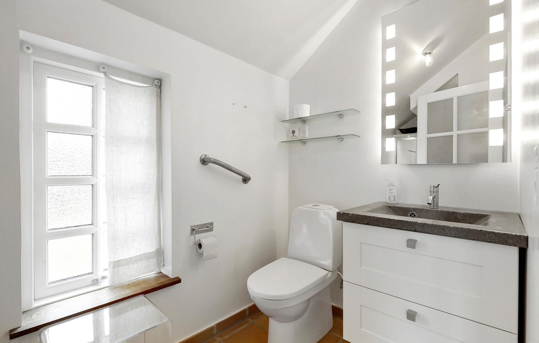 A bathroom with a toilet, a sink with a mirror, a towel rack, and a window with a curtain.