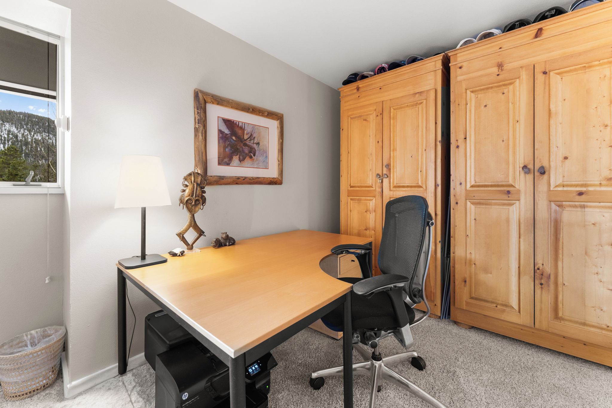 Una habitación con un escritorio de madera, una silla, una lámpara, un cuadro enmarco y un armario.