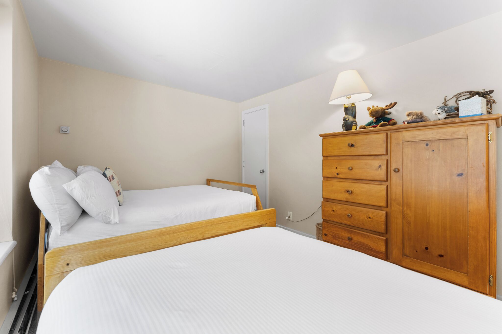 A bedroom with two beds, a wooden dresser, and a lamp.