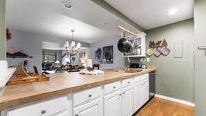 A modern kitchen with white cabinets, a wooden countertop, and a stainless steel sink. There are decorative items on the counter and a chandelier above. - Sj2503-3 (Keystone)