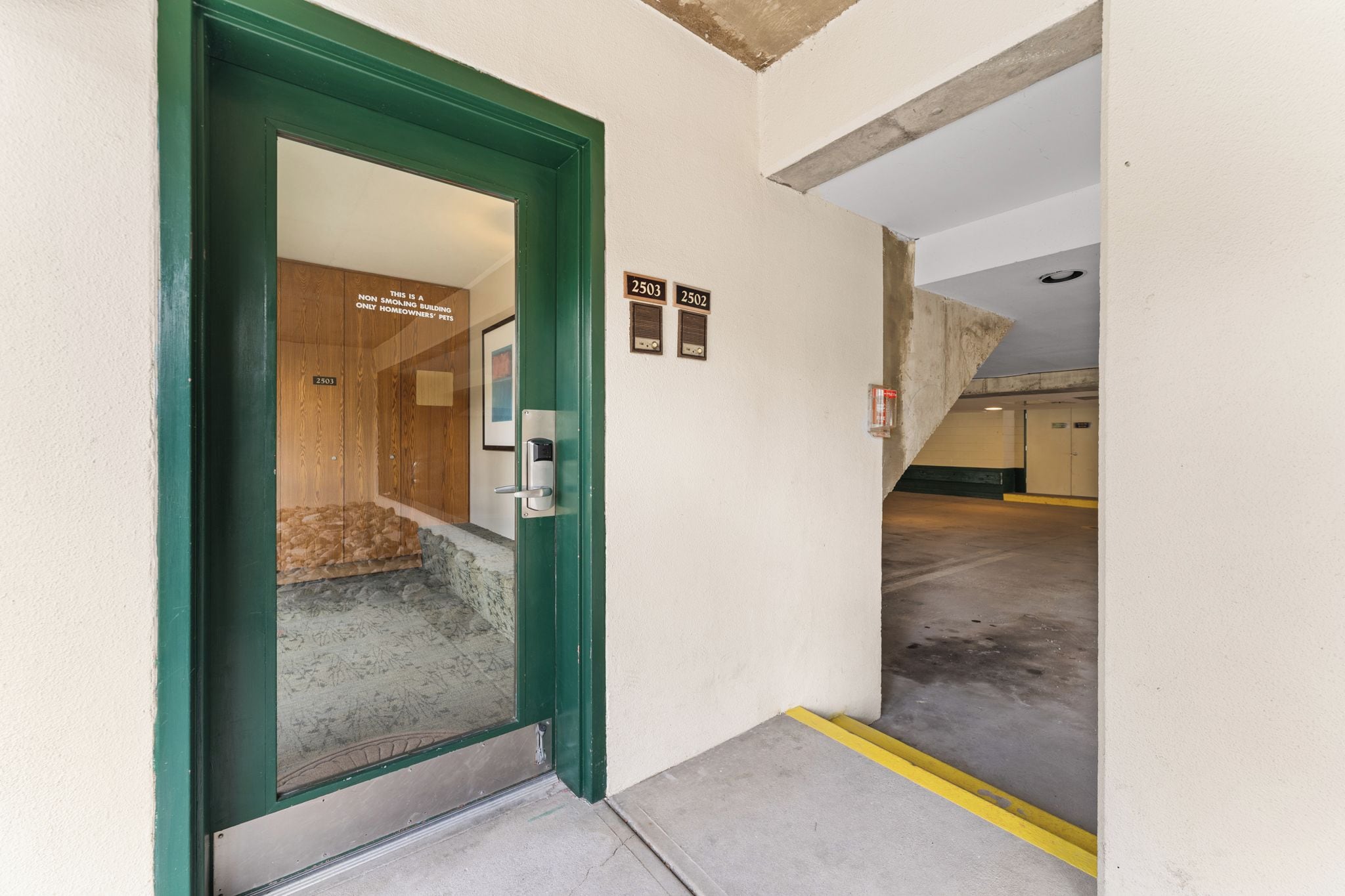 A parking garage entrance with a green door, numbered parking spots, and a concrete floor.