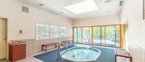 Une piscine intérieure spacieuse offrant une vue dégagée sur l’extérieur, dotée d’une verrière et d’un sol carrelé.