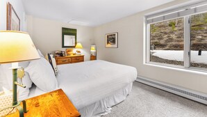 A bedroom with a large bed, bedside lamps, a dresser, and a window with a view of a snowy landscape. - Sj2503-3 (Keystone)