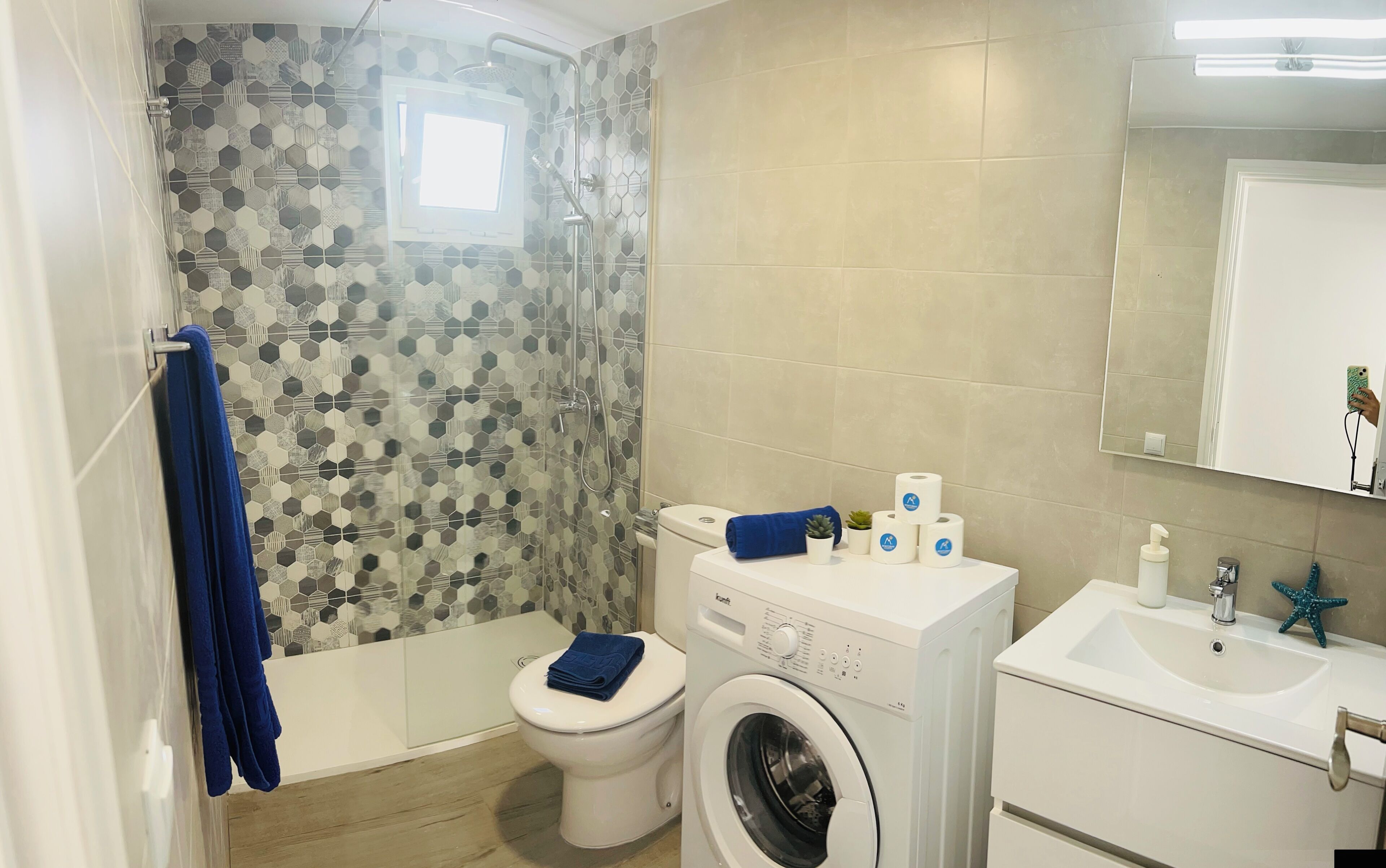 A bathroom with a shower, toilet, washing machine, and sink.