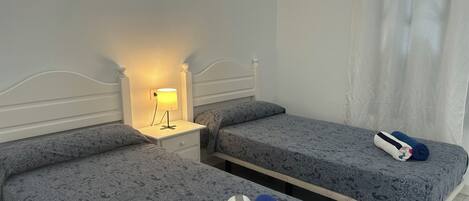 A hotel room with two single beds, a nightstand with a lamp, and a bathroom with a shower curtain.