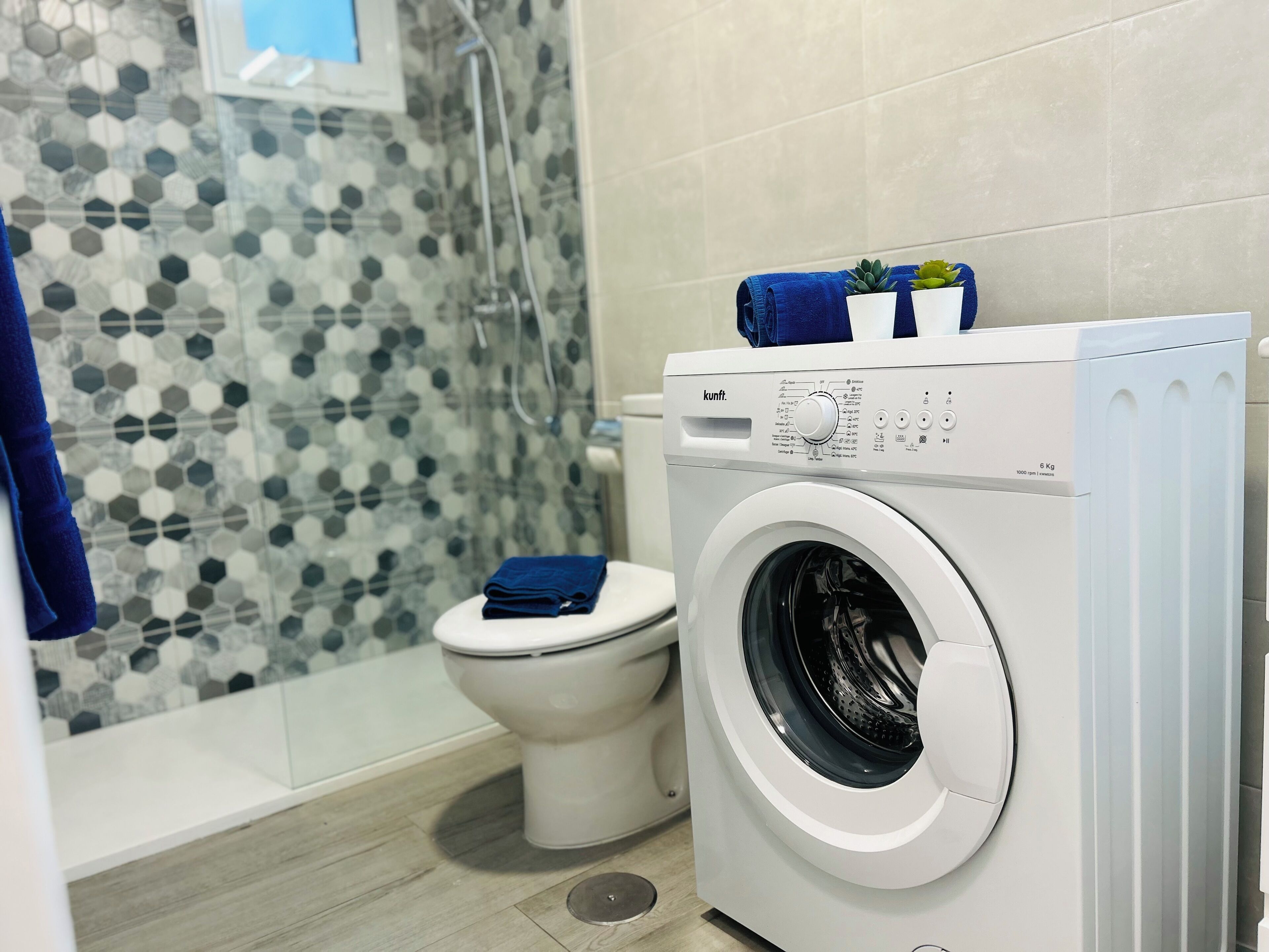 Un baño pequeño con lavadora, inodoro y zona de ducha.