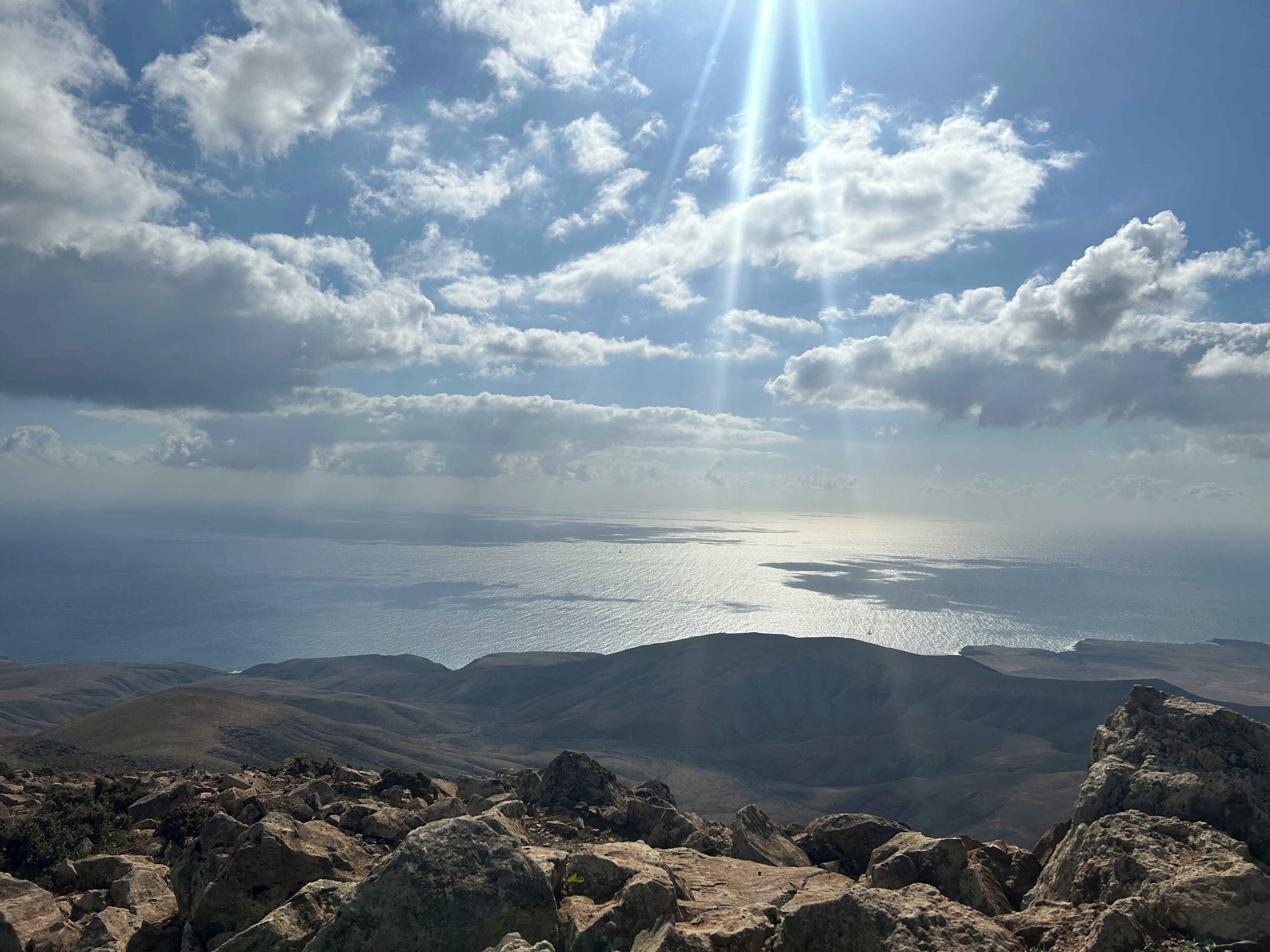A panoramic view of a mountainous landscape with a body of water in the distance, under a partly cloudy sky.