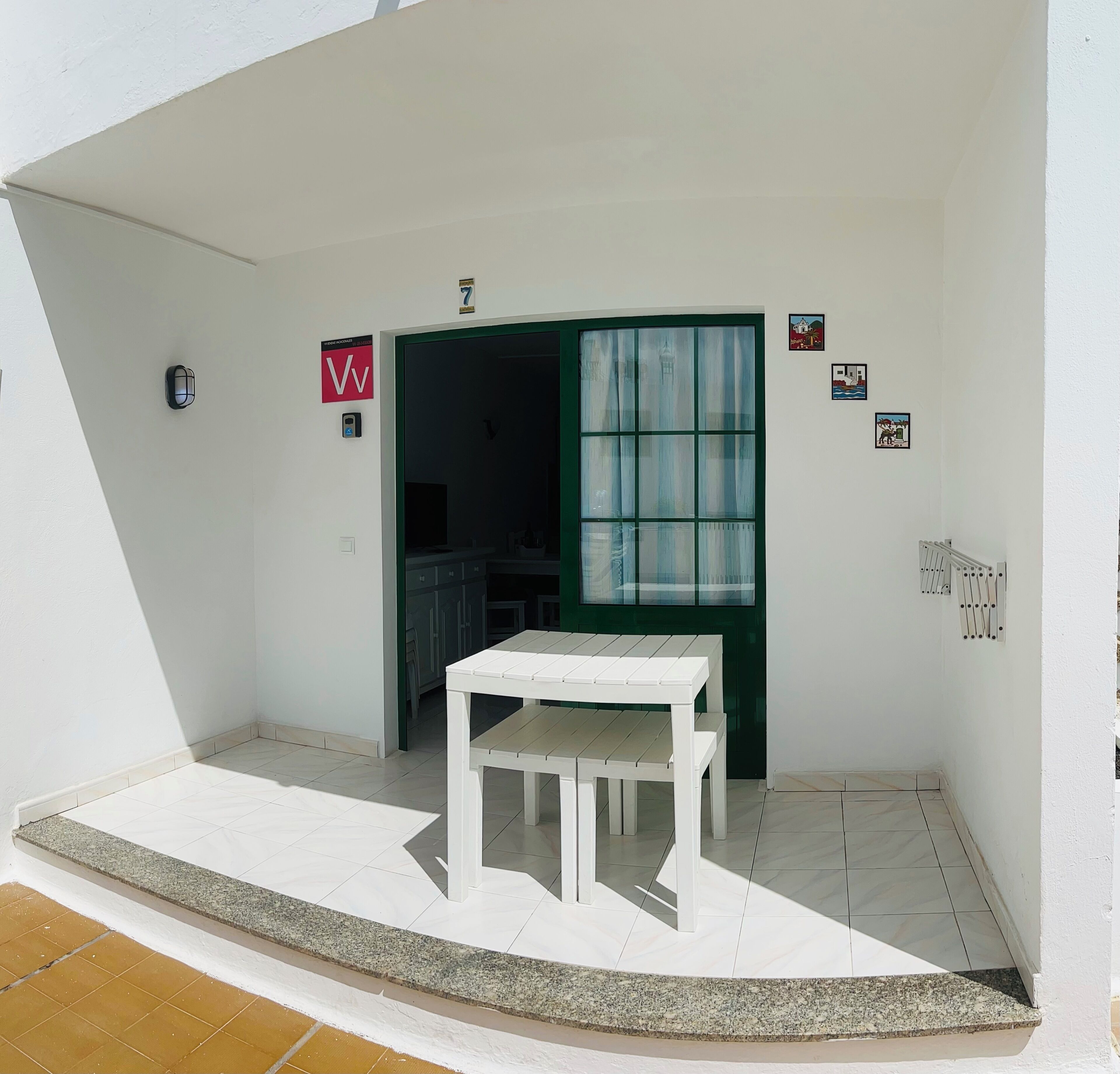 A white exterior wall with a door, a small table, and a window with curtains.