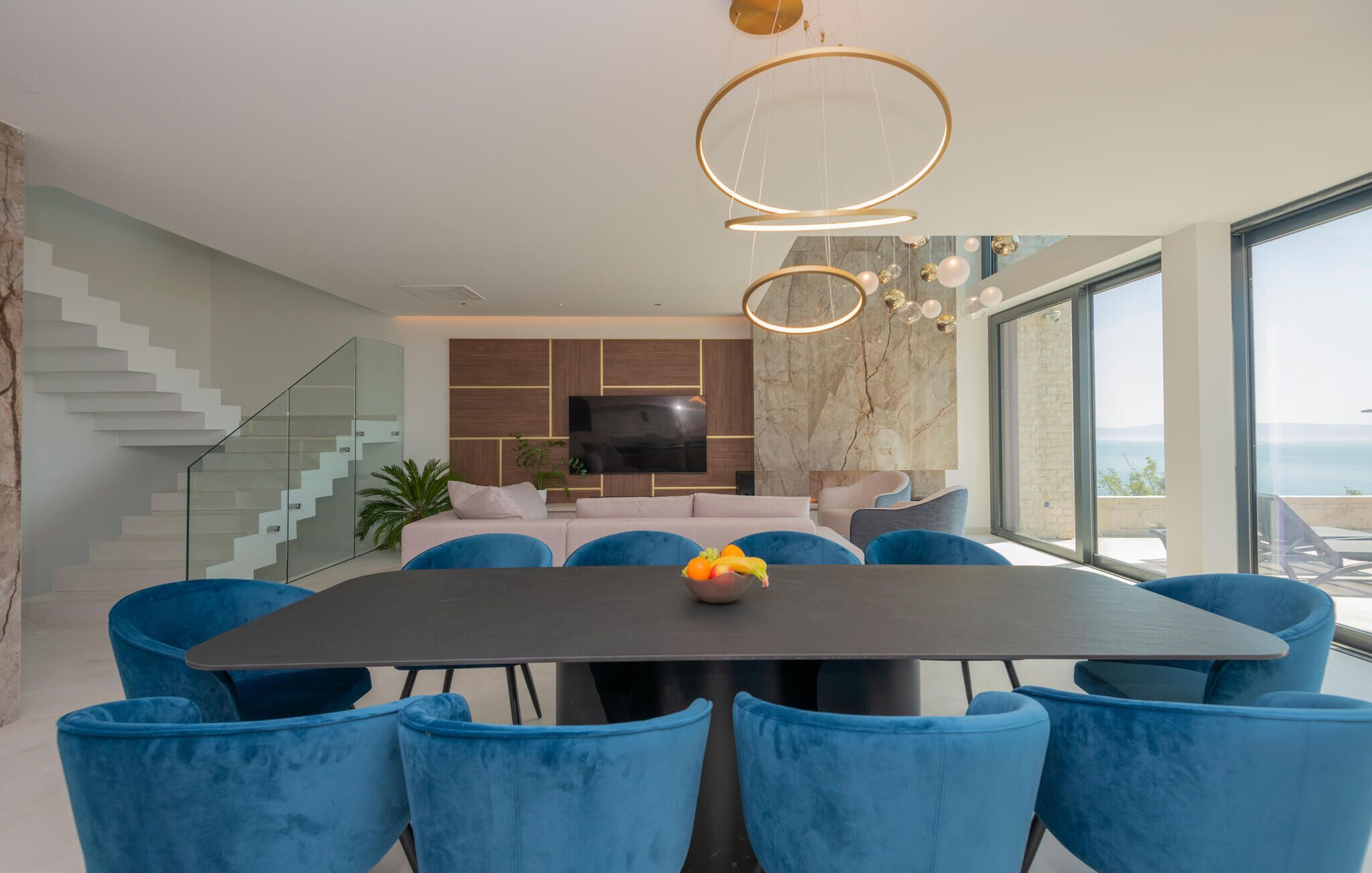 Un coin repas moderne avec une table sombre, des chaises en velours bleu et un saladier de fruits.