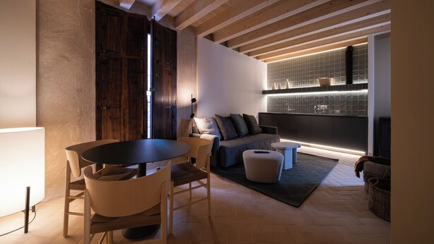 Un salon moderne avec un plafond en bois, un canapé, une table à manger avec des chaises et un coin cuisine avec un dosseret carrelé.