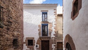Une rue étroite bordée d’immeubles en pierre, un bâtiment central doté d’une fenêtre bleue et d’un balcon, et un ciel dégagé.