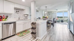 A modern kitchen with white cabinets, a dishwasher, and a dining area with a view.