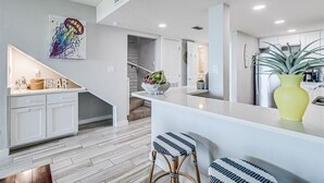 A modern kitchen with white cabinets, a bar area, and a staircase leading to a loft.