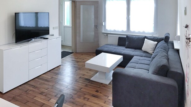 Ett modernt vardagsrum med en grå soffa, ett vitt soffbord och en tv som står på ett vitt skåp.