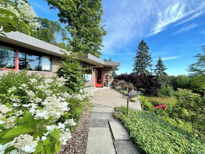 A modern house with a stone exterior, a red door, and a pathway leading to the entrance. - Nationally Registered Usonian Cottage at Lynn Hall by FLW's Fallingwater Builder (Port Allegany)
