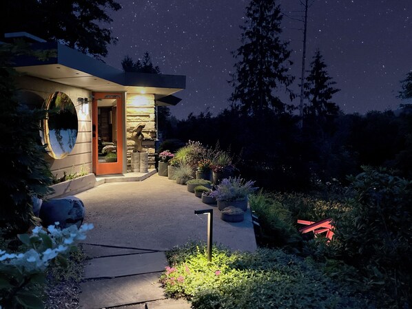 A modern house with a stone facade, a circular window, and a well-lit entrance. - Nationally Registered Usonian Cottage at Lynn Hall by FLW's Fallingwater Builder (Port Allegany)