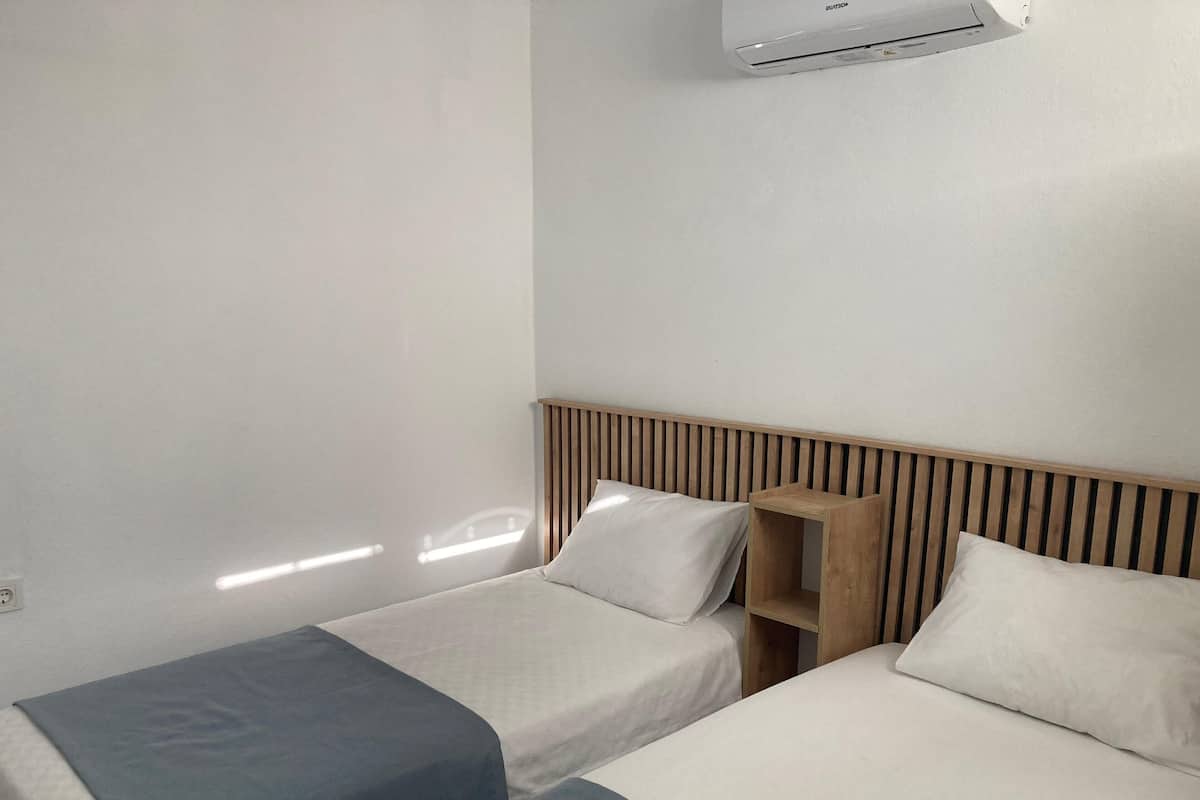 Habitación de hotel con dos camas individuales, cabecero de madera y unidad de aire acondicionado en la pared.