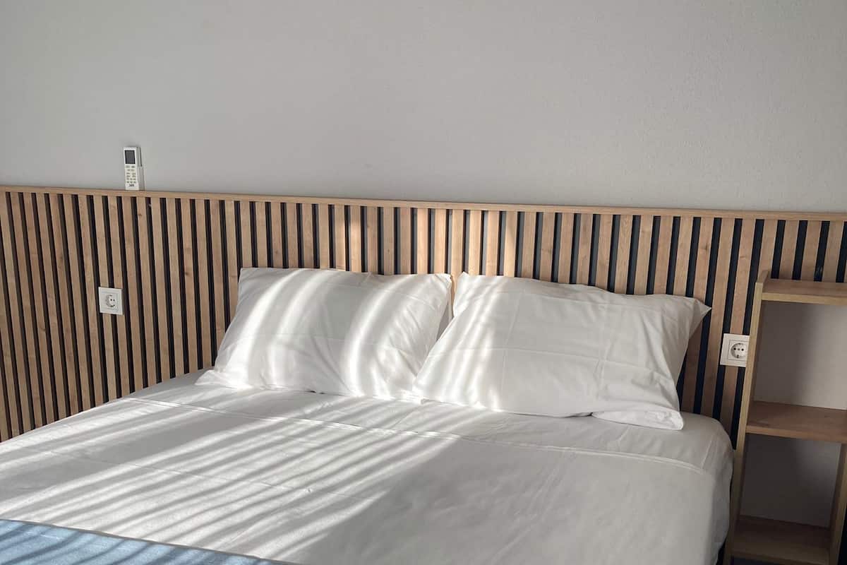 Una cama bien hecha con un cabecero de madera, una mesita de noche y un enchufe en la pared.