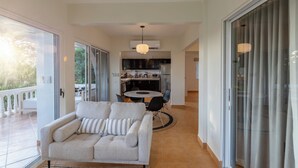A modern living room with a sofa, a dining table with chairs, a kitchen area with cabinets, and a sliding glass door leading to an outdoor balcony. - 2 BDR Ocean View Apt. in Pelada (Provincia de Guanacaste)