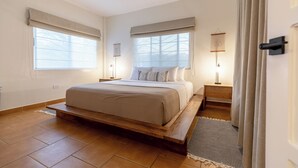 A bedroom with a bed, two bedside tables, a ceiling fan, and large windows with blinds. - 2 BDR Ocean View Apt. in Pelada (Provincia de Guanacaste)