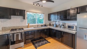 A modern kitchen with dark cabinetry, a built-in oven, a microwave, a refrigerator, and a window providing natural light. - 2 BDR Ocean View Apt. in Pelada (Provincia de Guanacaste)
