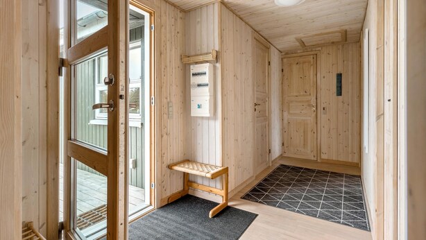 Ein Holzboden-Flur mit einer Sitzbank, einer Tür und einem Thermostat an der Wand.