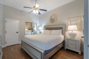 Une chambre à coucher comprenant un lit, une table de chevet, un miroir, un ventilateur de plafond et une porte.