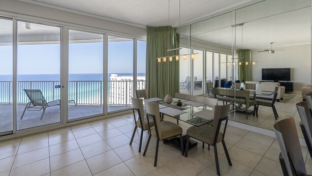 A spacious living area with a balcony overlooking the sea, a dining table with chairs, and a flat-screen TV. - Posh Beachfront Penthouse With Spectacular Gulf Views Tops'l Tides 1507 (Miramar Beach)