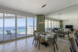 Un vaste espace de vie avec un balcon donnant sur la mer, une table à manger avec des chaises et un téléviseur à écran plat.