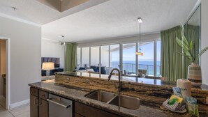 A modern kitchen with granite countertops, a double sink, and a view of a balcony with a dining area. - Posh Beachfront Penthouse With Spectacular Gulf Views Tops'l Tides 1507 (Miramar Beach)