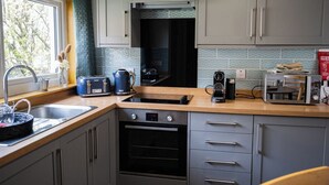 A modern kitchen with grey cabinets, a wooden countertop, a built-in oven, a coffee maker, and a toaster. - North Coast Cottage - Coastal Highland Retreat with Sea Views (Portgower)