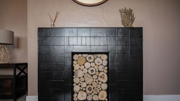 A fireplace with a stack of logs, a dark-colored mantel, and a decorative item on top. - North Coast Cottage - Coastal Highland Retreat with Sea Views (Portgower)