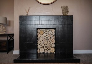 A fireplace with a stack of logs, a dark-colored mantel, and a decorative item on top. - North Coast Cottage - Coastal Highland Retreat with Sea Views (Portgower)