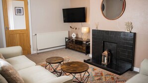 A living room with a fireplace, a television mounted on the wall, and a round mirror above it. - North Coast Cottage - Coastal Highland Retreat with Sea Views (Portgower)