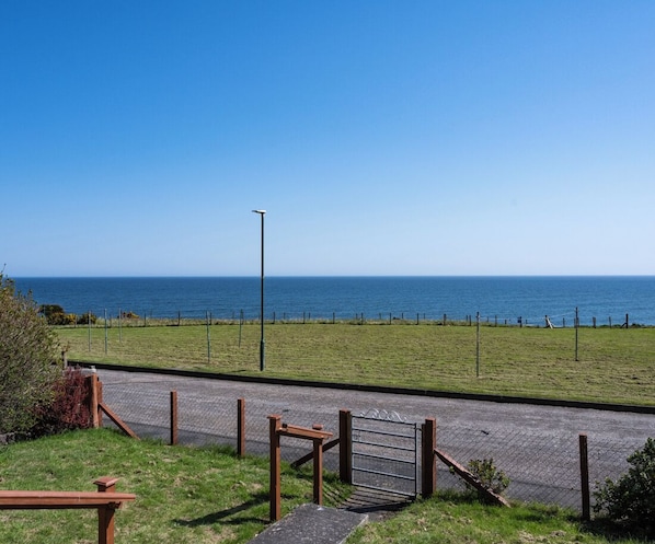 A coastal view with a paved pathway leading to a grassy area and a metal gate. - North Coast Cottage - Coastal Highland Retreat with Sea Views (Portgower)