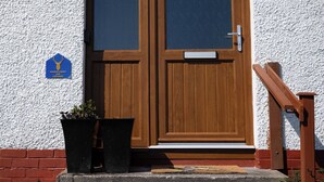 A wooden double door with a mailbox, a potted plant, and a wooden handrail. - North Coast Cottage - Coastal Highland Retreat with Sea Views (Portgower)